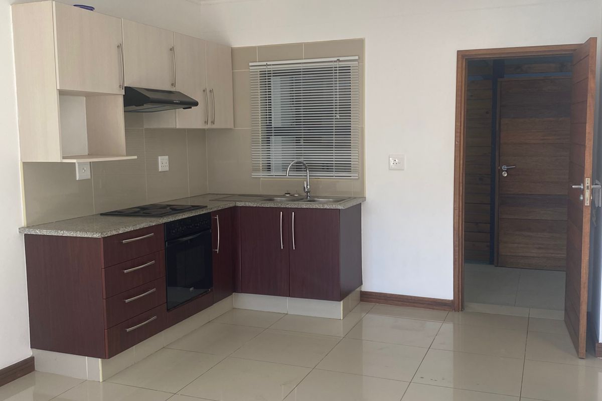 A compact kitchen featuring two-tone cabinetry, granite countertops, a built-in oven and hob, and tiled flooring, leading into an adjacent room.