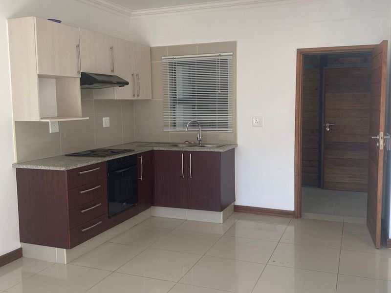 A compact kitchen featuring two-tone cabinetry, granite countertops, a built-in oven and hob, and tiled flooring, leading into an adjacent room.