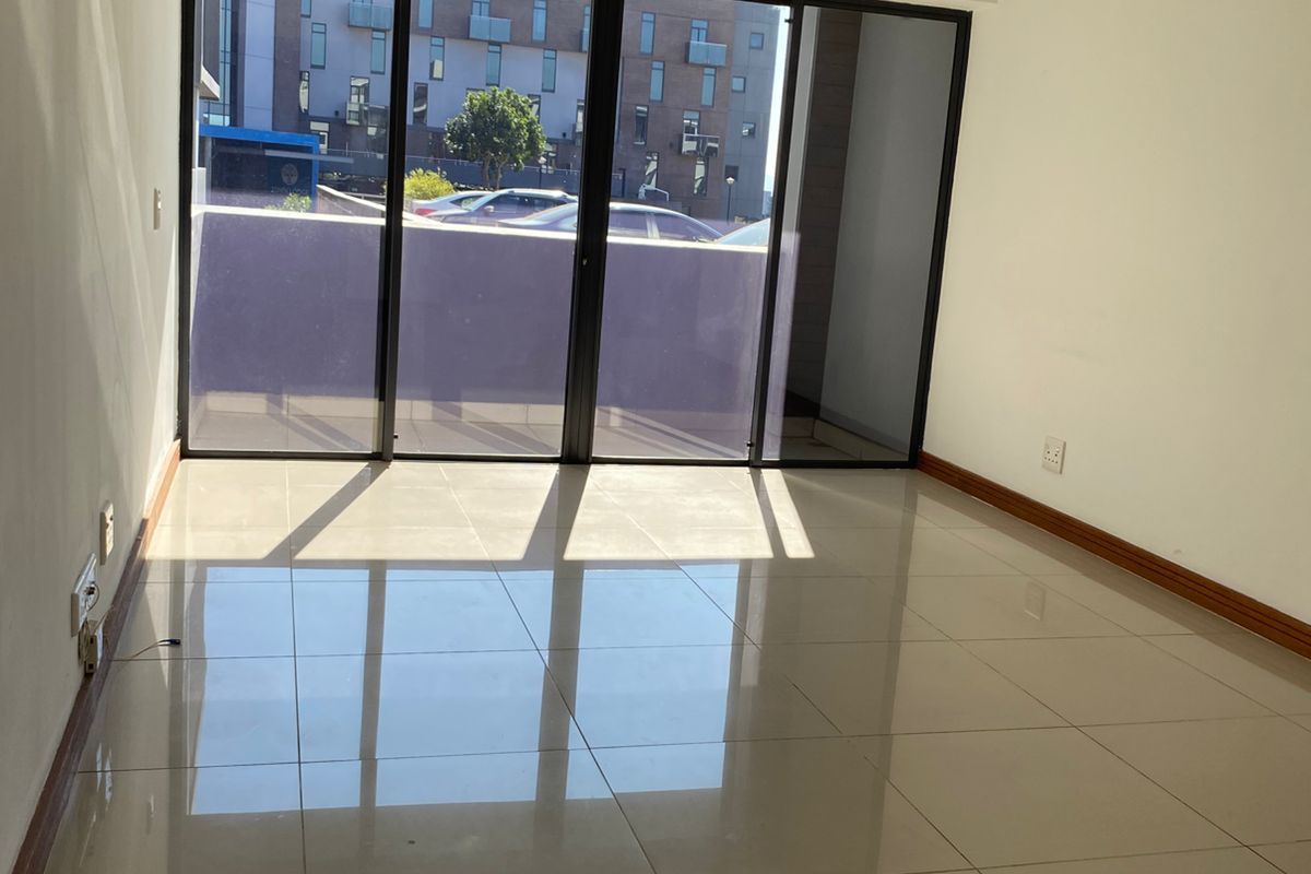A bright, empty living area featuring polished porcelain floor tiles, crown molding, and large sliding glass doors leading to an outdoor space.