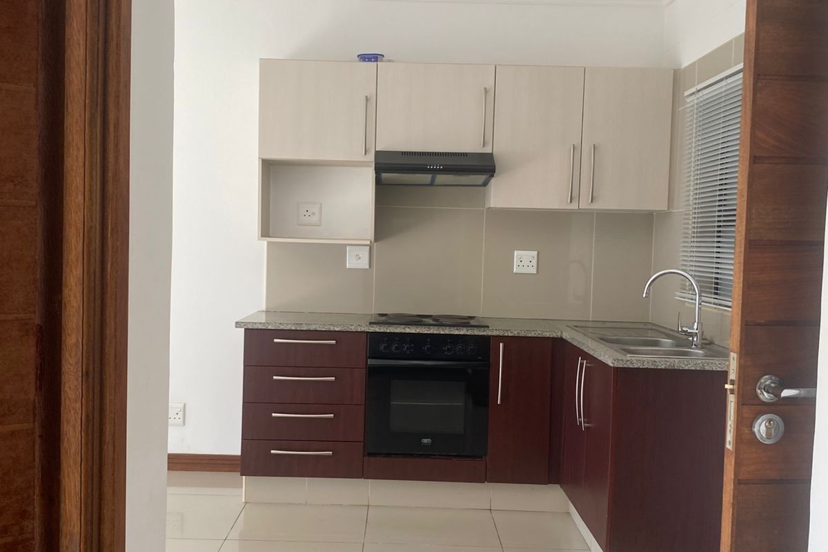 A compact, modern kitchen featuring two-tone cabinetry, a built-in oven, hob, extractor fan, and tiled flooring, viewed through a doorway.