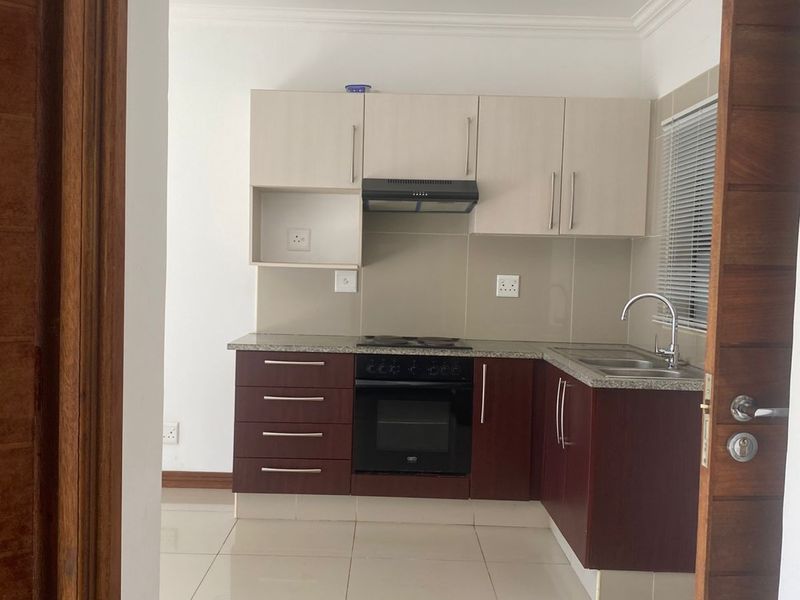 A compact, modern kitchen featuring two-tone cabinetry, a built-in oven, hob, extractor fan, and tiled flooring, viewed through a doorway.