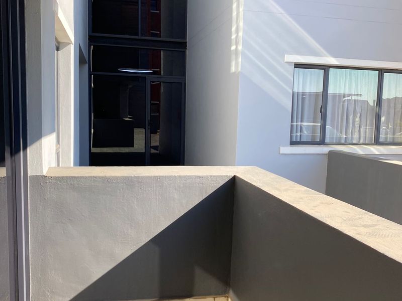 A modern, tiled balcony area with clean lines, featuring grey painted walls and large glass windows overlooking the building exterior.