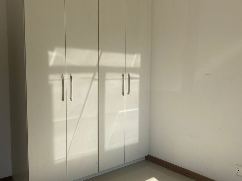 A bright bedroom featuring built-in floor-to-ceiling white cabinetry and neutral tiled flooring.