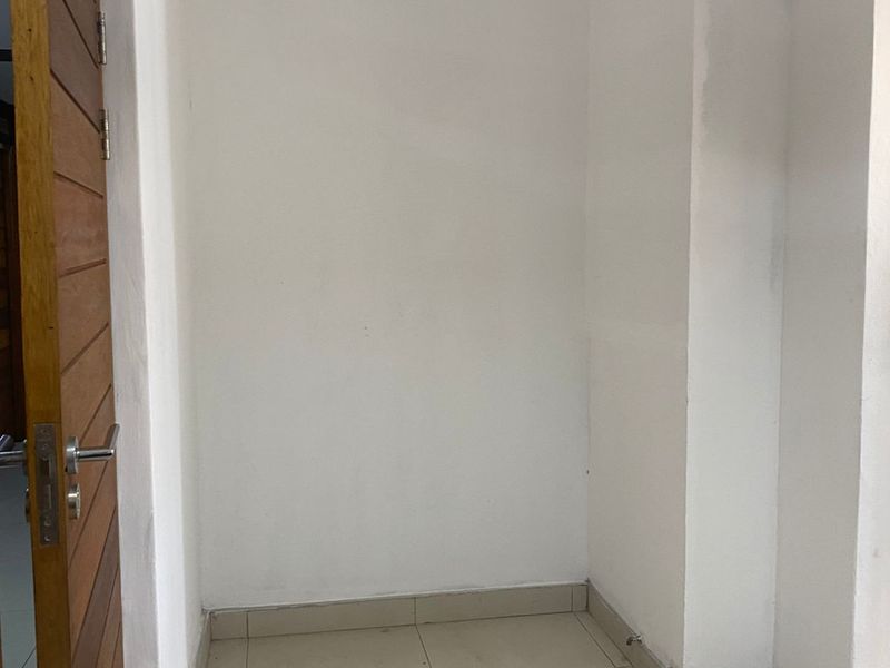 A small, empty utility space featuring tiled flooring and exposed plumbing connections, suitable for a laundry setup or additional storage.