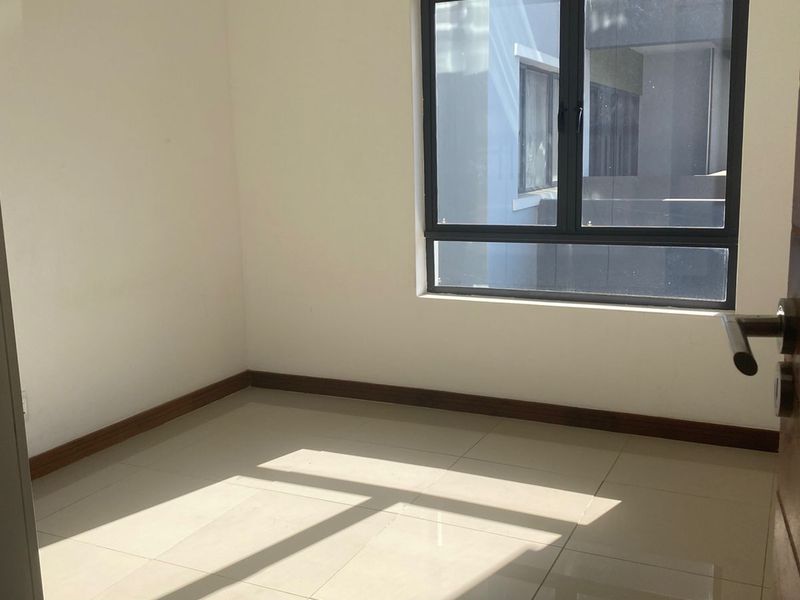 A bright, empty bedroom featuring neutral tiled flooring, white walls, and a modern dark-framed window providing natural light.
