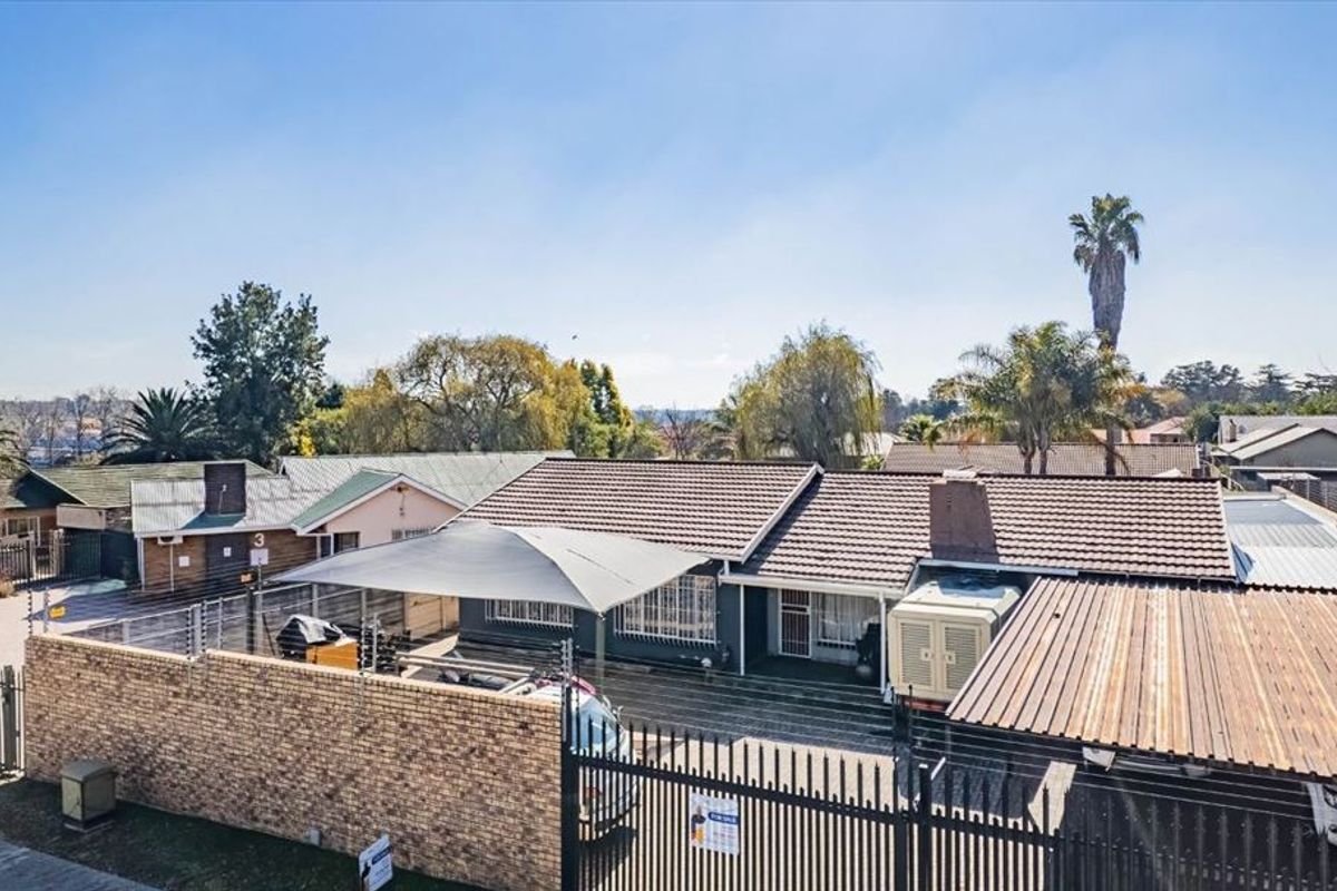 Aerial view of a residential property featuring a tiled roof, paved driveway, shade-cloth carport, perimeter brick wall, and security fencing.