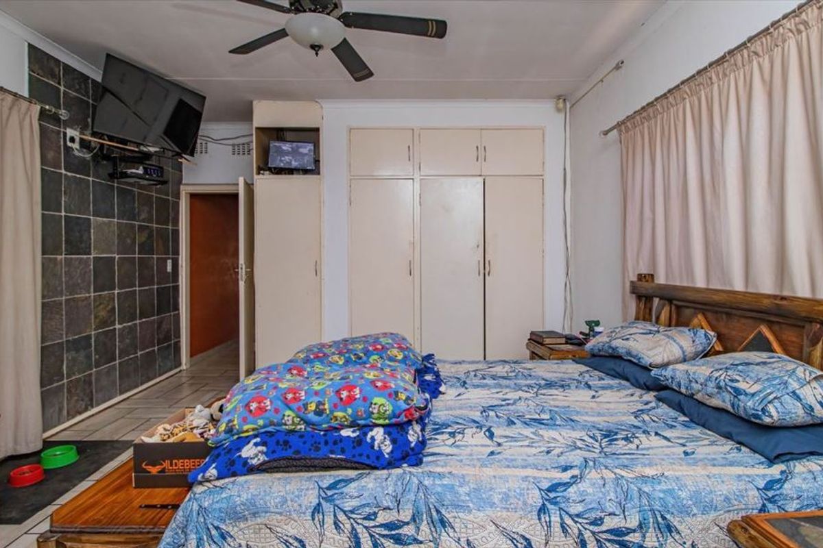 A bedroom featuring built-in cupboards, a ceiling fan, and a feature wall with stone-style tiling.