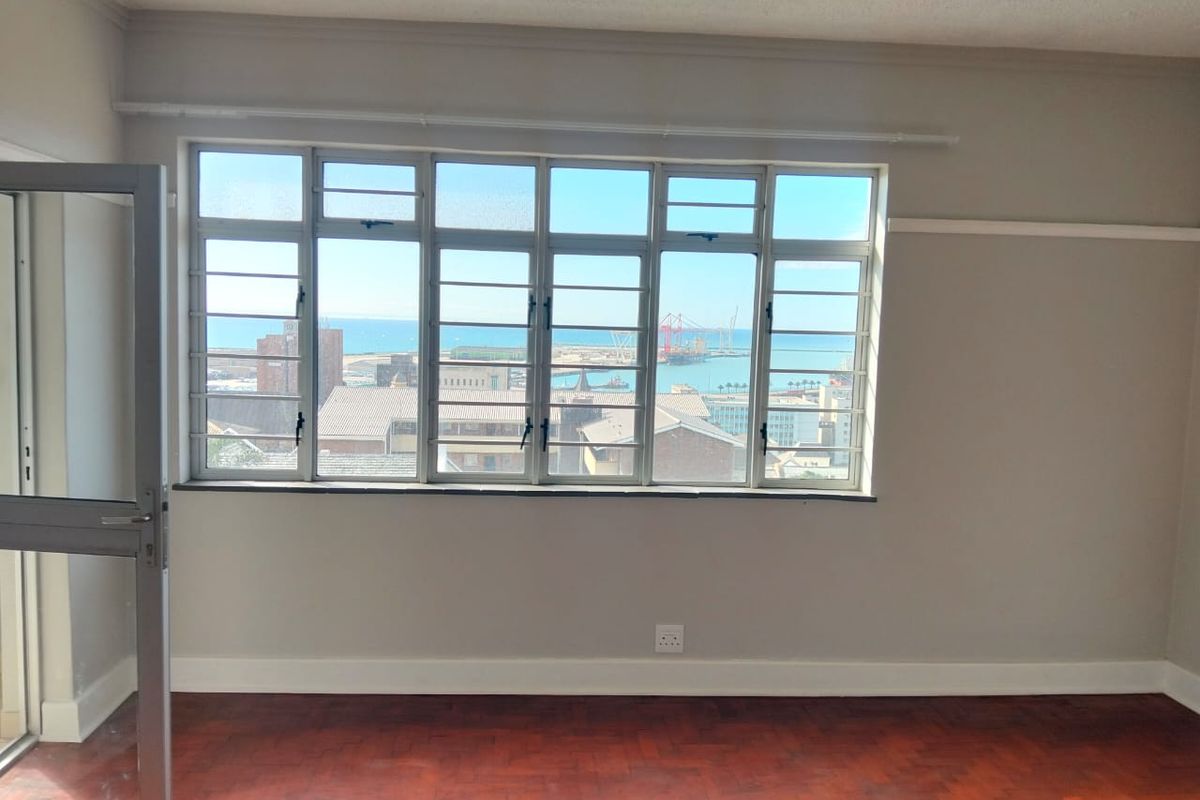 An empty bedroom featuring original parquet flooring, large steel-framed windows, and elevated views of the harbor and city.