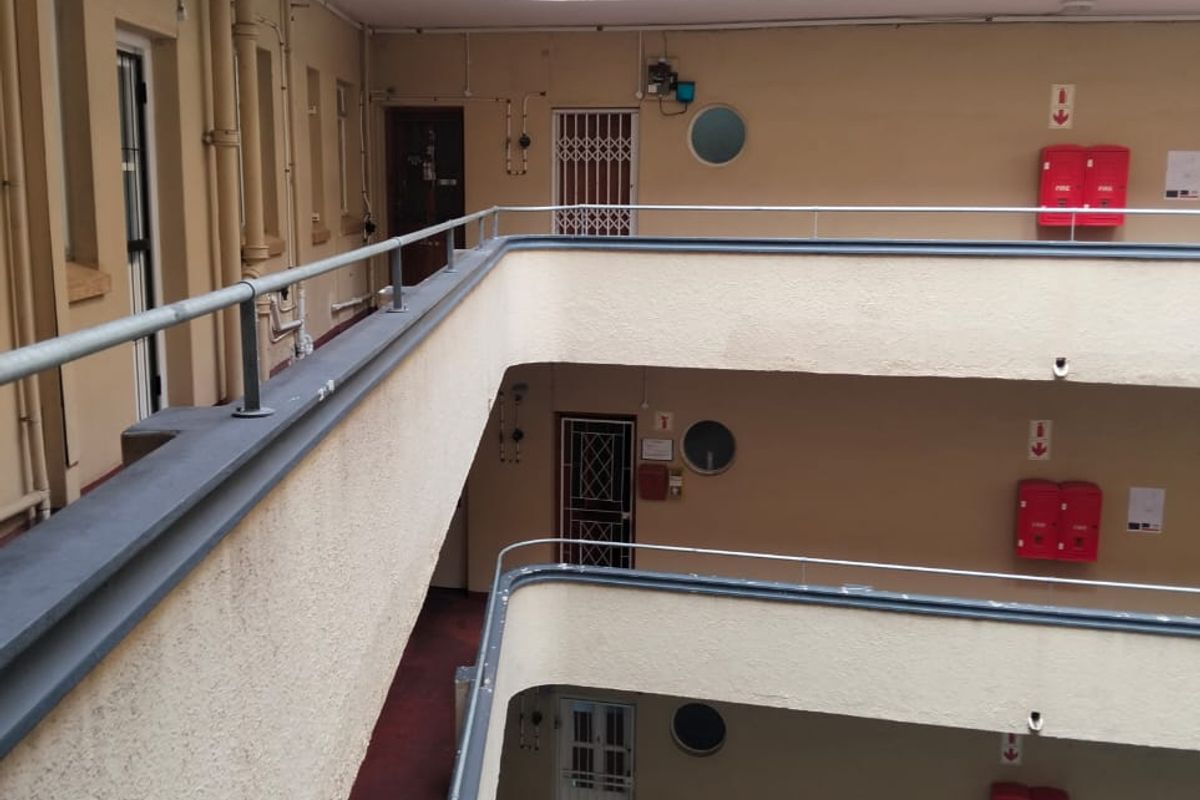 View of an apartment building's open-air central corridor featuring metal railings, security gates, and fire safety equipment on multiple levels.