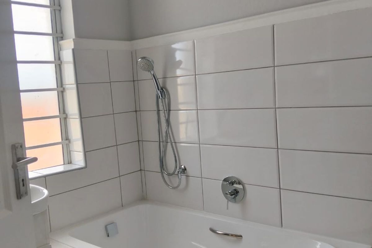 A clean, modern bathroom featuring a built-in bathtub with a handheld shower attachment and white ceramic wall tiling.
