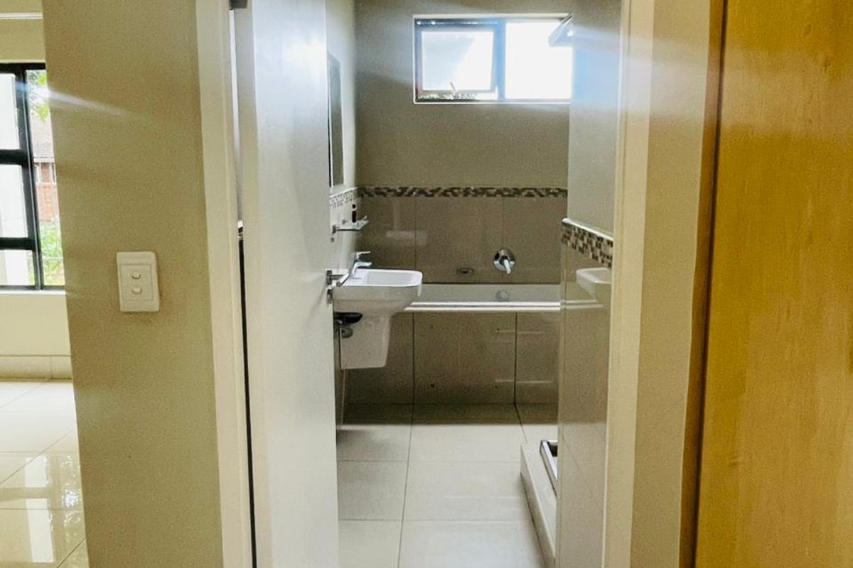 A view into a functional bathroom featuring tiled flooring, a wall-mounted basin, and a bathtub with a tiled splashback.