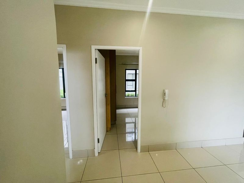 A bright hallway featuring neutral tiled flooring and an intercom system, providing access to adjacent rooms with natural light.