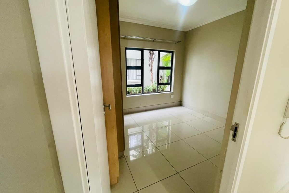 A bright, empty bedroom featuring neutral tiled flooring, a large window with natural light, and a built-in cupboard.