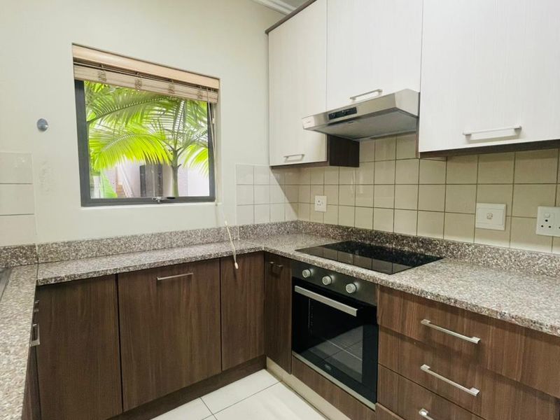 A functional kitchen featuring two-tone cabinetry, granite countertops, a built-in oven, electric hob, and an extractor fan with tiled flooring.