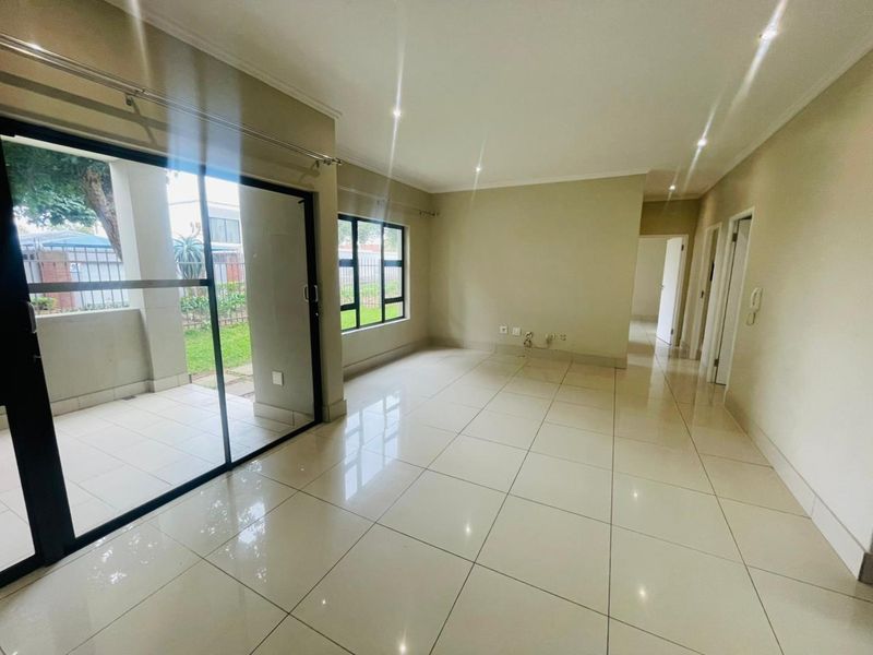 Spacious open-plan living area featuring large format floor tiles, recessed downlighting, and sliding glass doors providing direct access to a private patio.