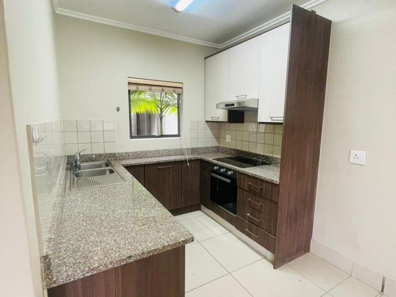 A functional kitchen featuring granite countertops, built-in cabinetry, an integrated oven, hob, and extractor fan with tiled flooring.