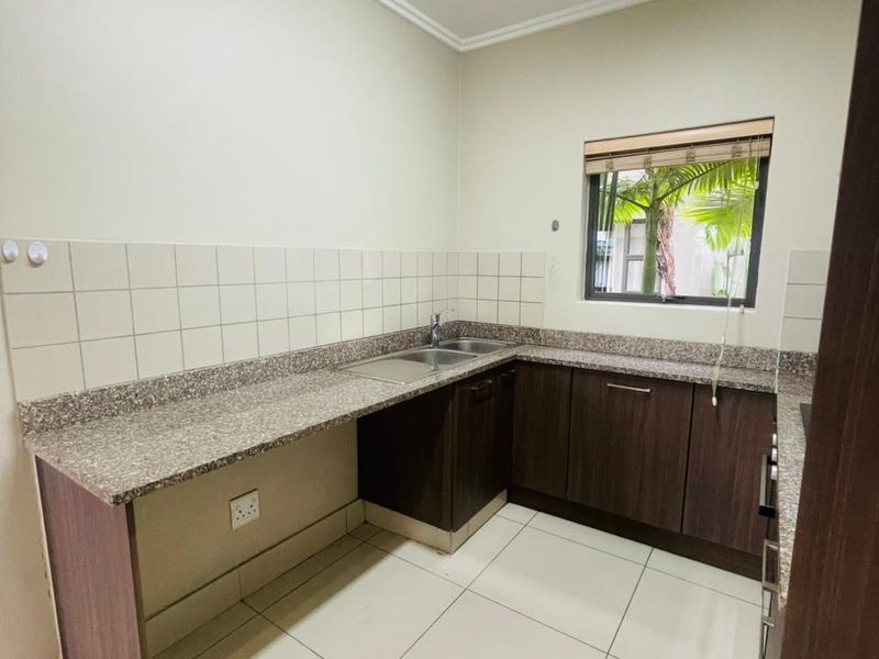 A functional kitchen featuring dark wood cabinetry, granite countertops, tiled splashbacks, and a double sink, with tiled flooring throughout.