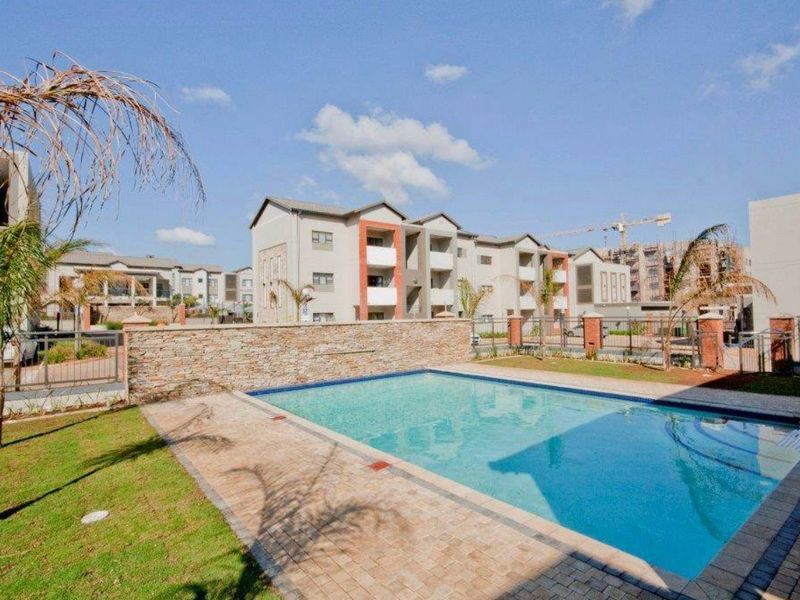 A well-maintained communal swimming pool area featuring paved surrounds, stone-clad feature wall, and landscaped garden space within a modern apartment complex.