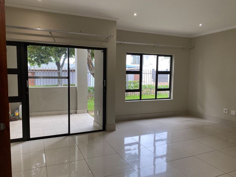 Bright and spacious living area featuring polished porcelain floor tiles, recessed downlighting, and large sliding glass doors leading to a private patio.