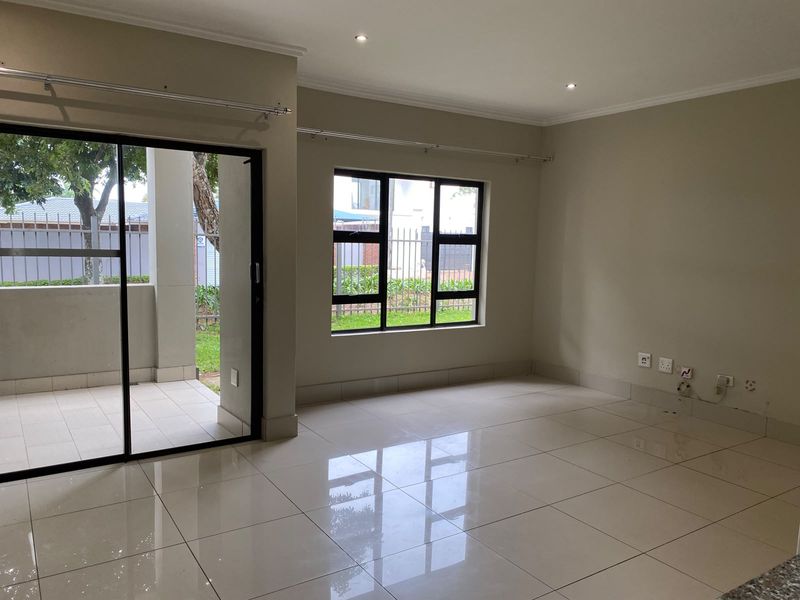Bright and spacious open-plan living area featuring polished porcelain floor tiles, recessed downlighting, and large sliding glass doors leading to a private patio.