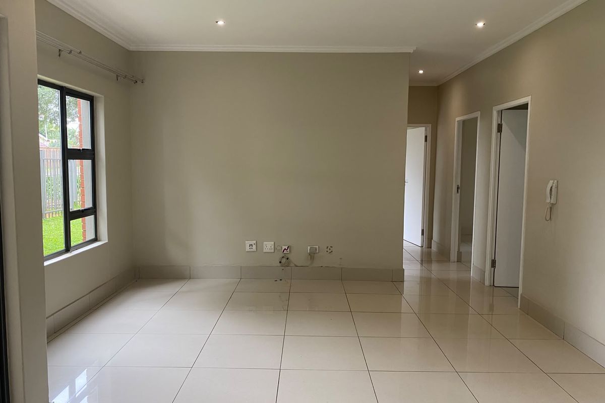 A bright, empty living area featuring neutral tiled flooring, recessed ceiling lighting, and multiple doorways leading to other parts of the apartment.
