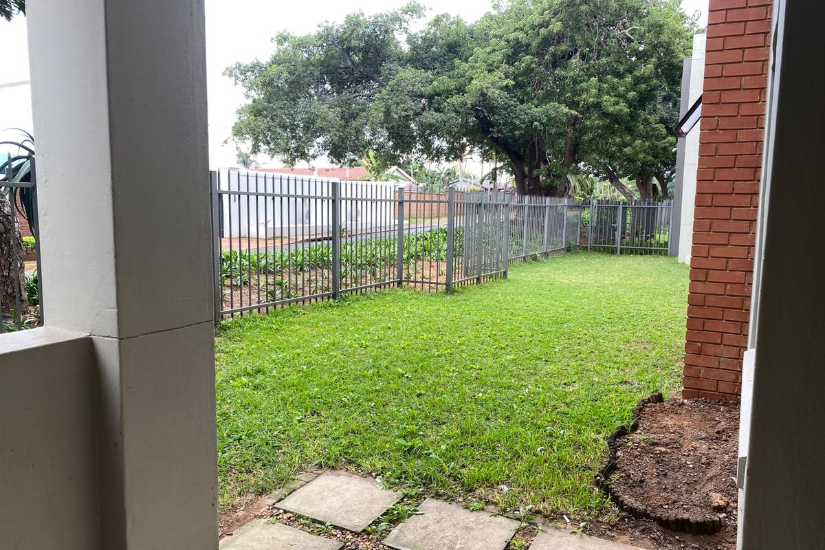 A private rear garden area featuring a manicured lawn, paved stepping stones, and secure perimeter metal fencing.