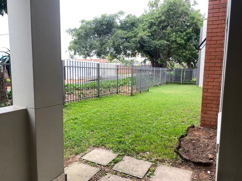 A private rear garden area featuring a manicured lawn, paved stepping stones, and secure perimeter metal fencing.