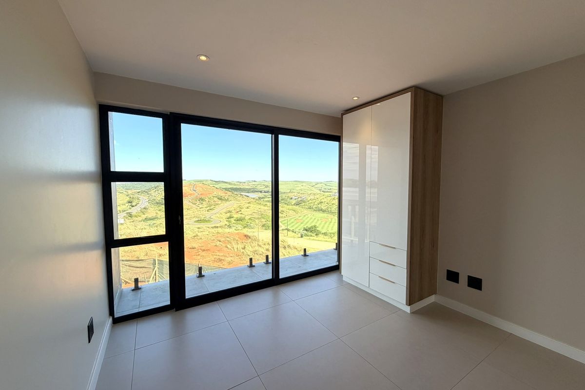 Modern bedroom featuring large floor-to-ceiling windows with scenic landscape views, built-in cabinetry, and neutral tiled flooring.