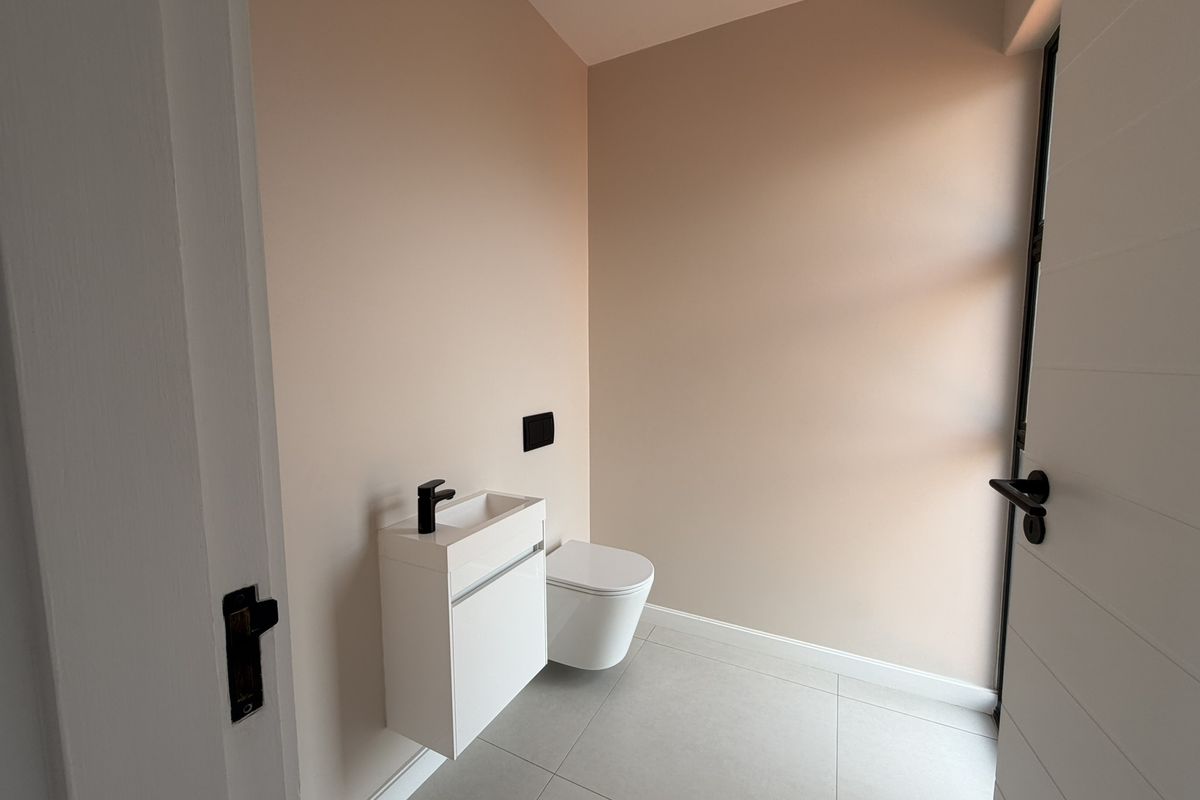 A modern, minimalist powder room featuring a wall-mounted vanity with a sleek basin, a wall-hung toilet, and neutral-toned tiled flooring.