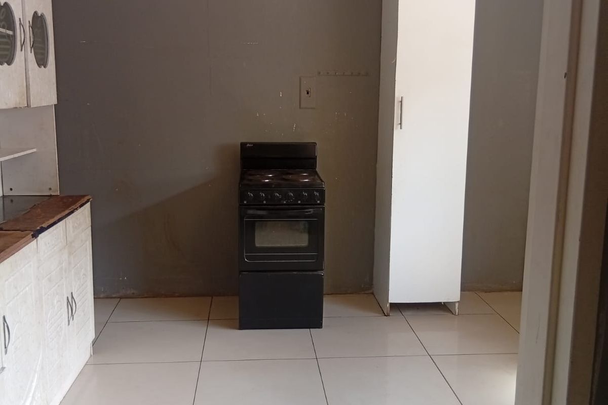A basic kitchen area featuring tiled flooring, white cabinetry, and a freestanding electric stove against a grey wall.