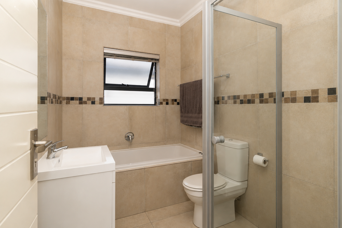 A well-maintained bathroom featuring neutral wall tiles, a built-in bathtub, a modern vanity, and a glass-enclosed shower area.