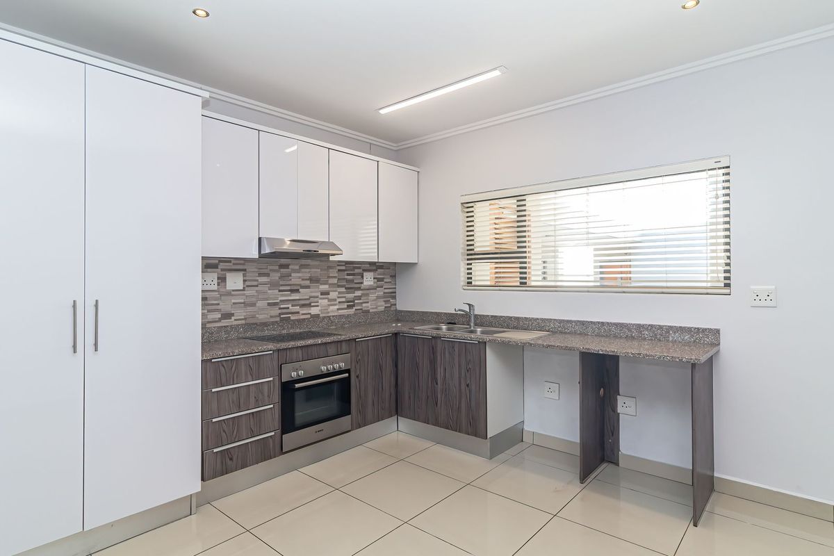 Modern kitchen featuring white and wood-grain cabinetry, granite countertops, built-in oven, hob, extractor fan, and tiled flooring in a clean, well-lit space.