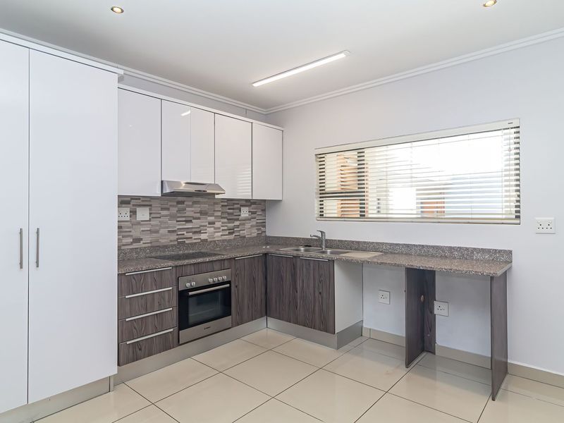 Modern kitchen featuring white and wood-grain cabinetry, granite countertops, built-in oven, hob, extractor fan, and tiled flooring in a clean, well-lit space.