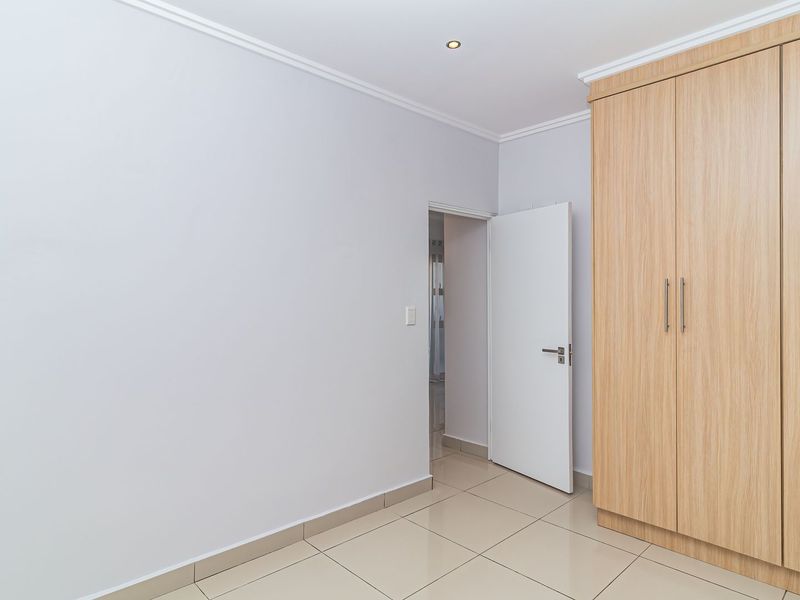 A clean, empty bedroom featuring light-toned built-in cupboards, neutral tiled flooring, and recessed ceiling lighting.