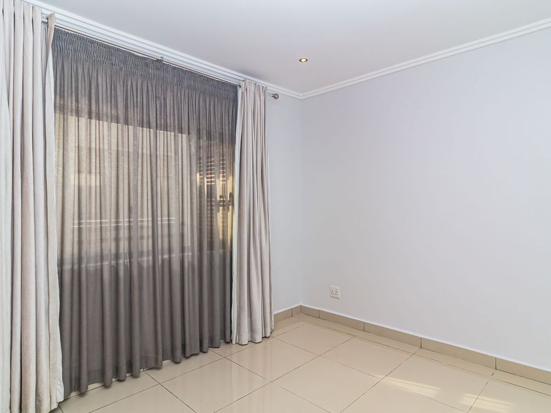 A bright, empty bedroom featuring neutral tiled flooring, recessed downlighting, and installed curtain tracks, providing a clean and versatile space.