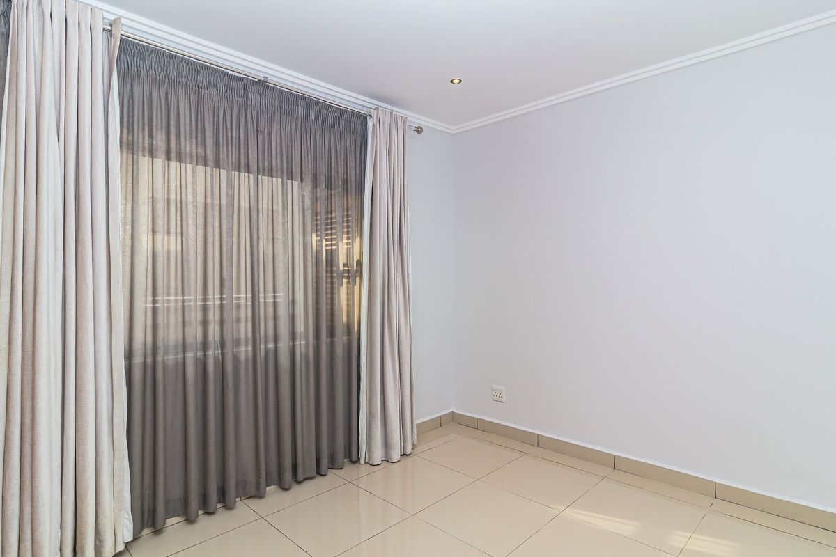 A bright, empty bedroom featuring neutral tiled flooring, recessed downlighting, and installed curtain tracks, providing a clean and versatile space.