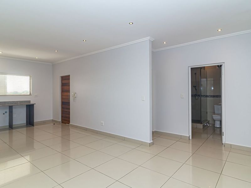 Spacious open-plan living area featuring tiled floors, recessed lighting, and a compact kitchen nook, with an adjacent bathroom accessible via a doorway.