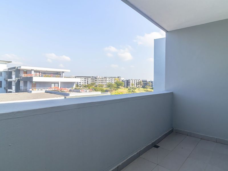A clean, empty balcony featuring tiled flooring and a solid balustrade, offering an open view of the surrounding apartment complex.