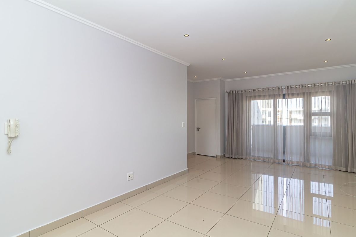 A bright, spacious, and empty living area featuring neutral tiled flooring, recessed lighting, and a large sliding glass door leading to an outdoor space.