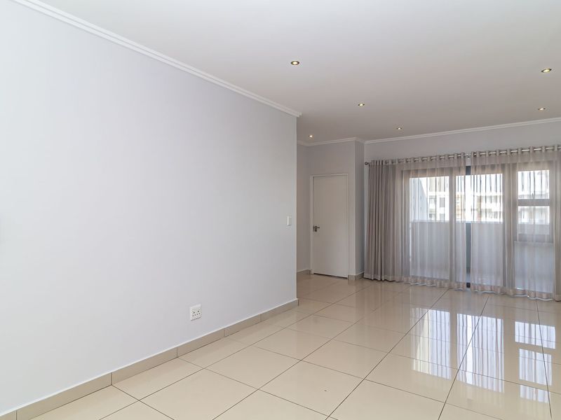 A bright, spacious, and empty living area featuring neutral tiled flooring, recessed lighting, and a large sliding glass door leading to an outdoor space.