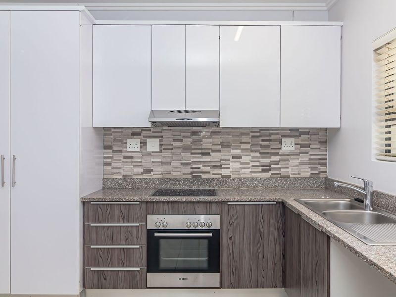 Modern kitchen featuring two-tone cabinetry, granite countertops, a mosaic tile backsplash, and integrated stainless steel appliances including an oven and hob.