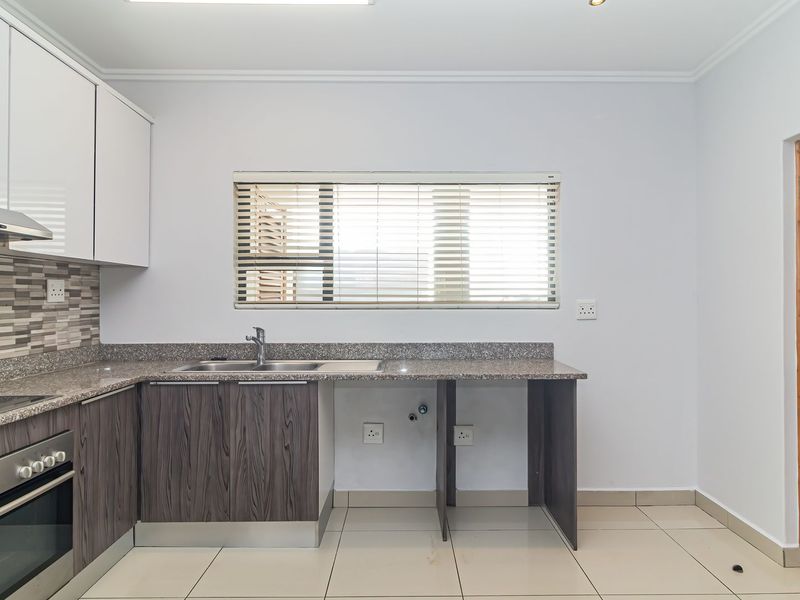 Modern kitchen featuring granite countertops, built-in oven, extractor fan, and ample cabinetry with tiled flooring and a neutral finish.