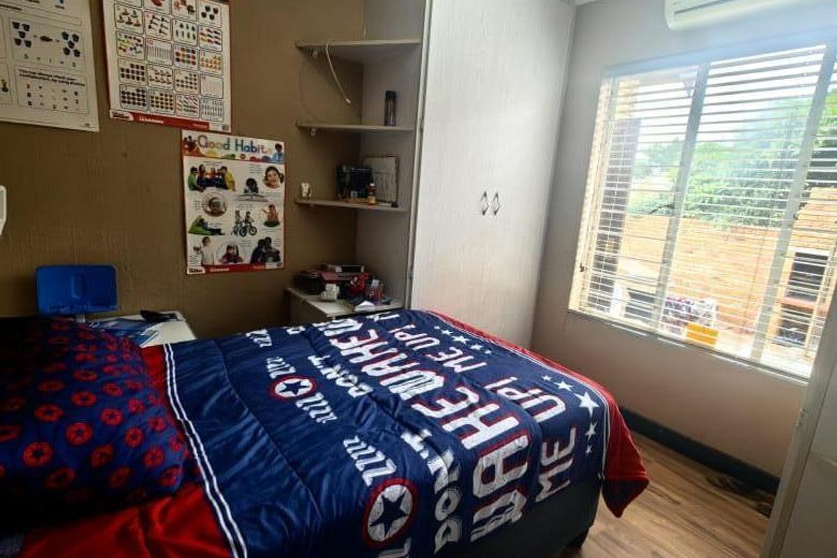 A functional bedroom featuring built-in cupboards, laminate flooring, a wall-mounted air conditioning unit, and window blinds.