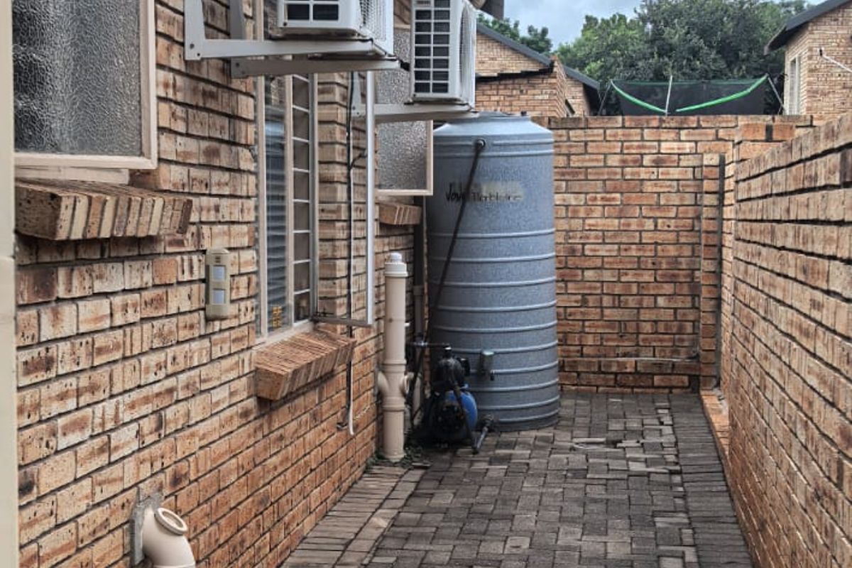 Side exterior walkway featuring brick paving, wall-mounted air conditioning units, and a water storage tank with pump infrastructure.
