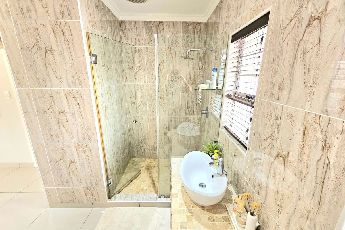 Modern bathroom featuring floor-to-ceiling marble-look tiling, a glass-enclosed walk-in shower, and a contemporary vessel sink vanity.