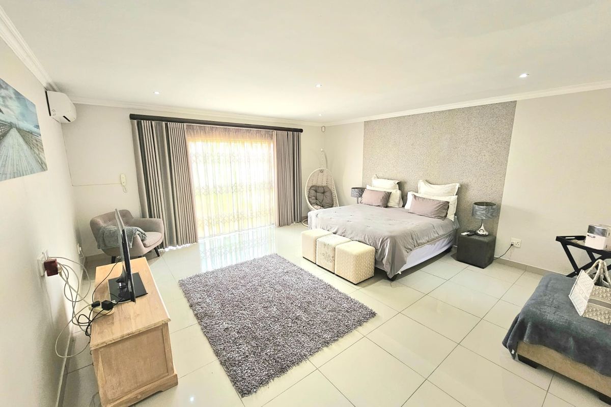 Spacious bedroom featuring large format floor tiles, recessed downlighting, a textured feature wall, and sliding glass doors leading to the exterior.