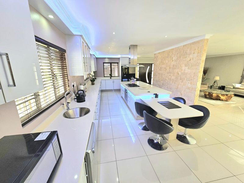 Modern open-plan kitchen featuring a large central island with integrated cooktop, stone countertops, sleek cabinetry, and recessed LED lighting throughout.