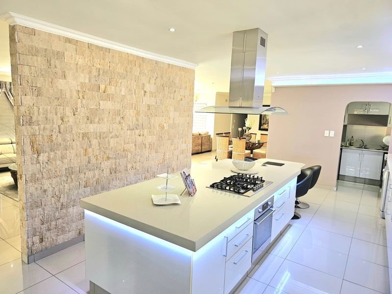 Modern open-plan kitchen featuring a large central island with built-in gas hob, oven, and stainless steel extractor fan, complemented by sleek cabinetry.