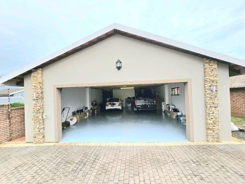 A spacious double garage featuring a paved driveway, stone-clad pillars, and a clean epoxy-coated floor, providing ample secure parking and storage space.
