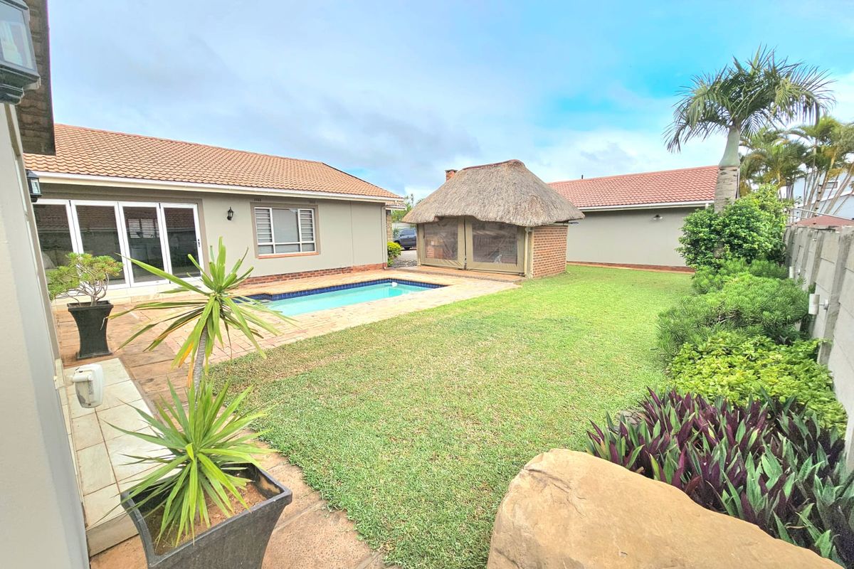 Spacious rear garden featuring a swimming pool, paved patio area, and a traditional thatched lapa structure, perfect for outdoor entertaining.
